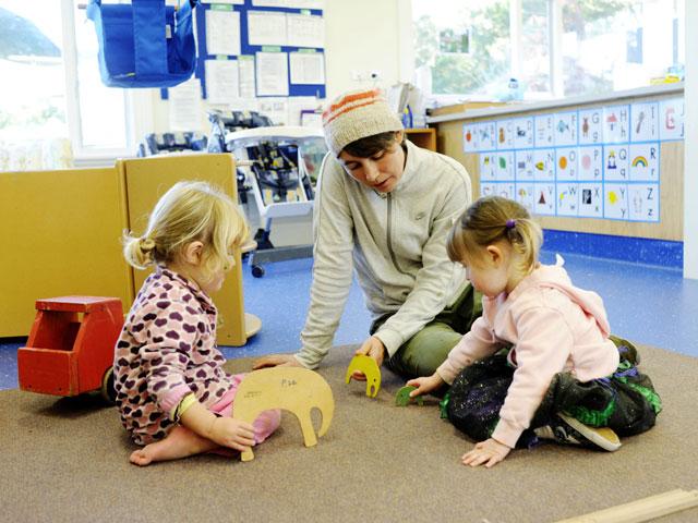 2 children and teacher playing on carpeted floor